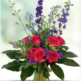 Pink roses and purple flowers arranged in a clear glass vase