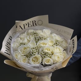 Bouquet of white roses wrapped in cream paper with a ribbon