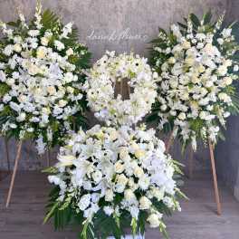 White floral funeral wreaths and sprays on stands with a large floor arrangement