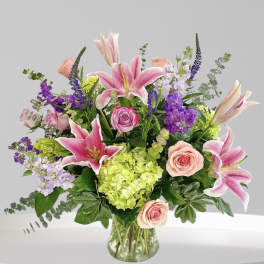 Mixed bouquet of pink lilies, roses, and purple flowers in a glass vase