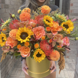 Large orange and yellow floral arrangement in a gold box