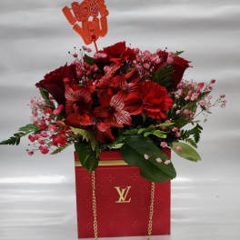 Red floral arrangement in a branded gift bag with an "I love you" topper