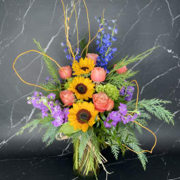 Bouquet of sunflowers, pink roses, and purple flowers in a glass vase