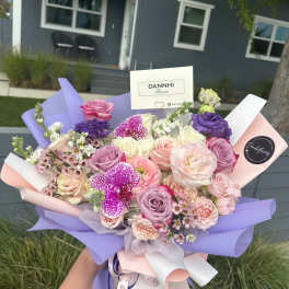 Handheld bouquet of pink, purple, and white flowers wrapped in pastel paper