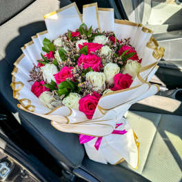 Bouquet of pink and white roses wrapped in white paper with gold trim