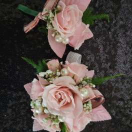 Two pink rose corsages with ribbon and pearl accents on a dark sequined background