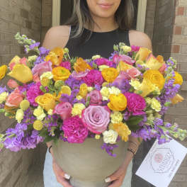 Large mixed bouquet in a beige hatbox with pink, yellow, and purple flowers