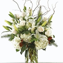 White roses and lilies in a clear glass vase with curly branches