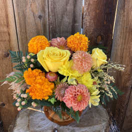 Bouquet of yellow roses, orange marigolds, and pink dahlias in an amber vase