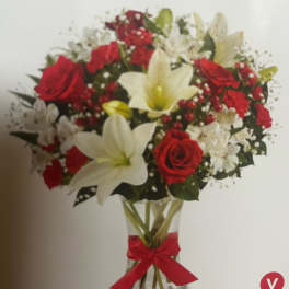 Bouquet of red roses and white lilies in a clear vase with a red ribbon