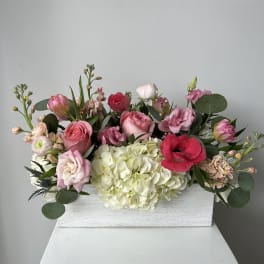 Mixed pink and white flowers arranged in a white wooden box