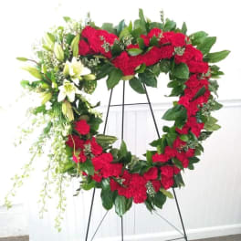 Heart-shaped floral wreath with red carnations and white lilies on a stand