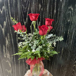 Red roses in a glass vase with greenery and a red ribbon