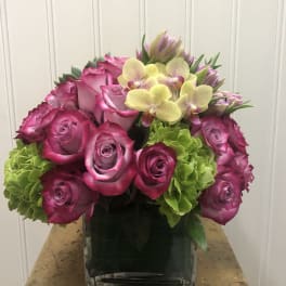Pink roses and green hydrangeas in a square glass vase with orchids