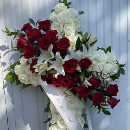 Cross-shaped floral spray of red and white roses with lilies and a memorial ribbon