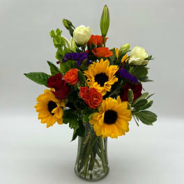 Mixed bouquet of sunflowers, roses, and lilies in a glass vase
