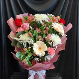 Mixed bouquet of pink and white flowers wrapped in pink paper with a white ribbon