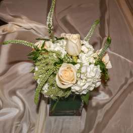 Small wedding centerpiece of ivory roses and white hydrangeas in a glass cube vase