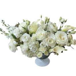 White floral arrangement in a blue glass vase with roses, calla lilies, and hydrangeas