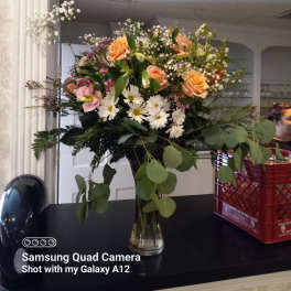 Mixed bouquet of peach roses, white daisies, and baby's breath in a glass vase