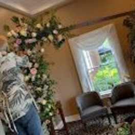 Floral arch with white and pink flowers in a room, with two people arranging it