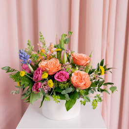 Mixed bouquet of peach, pink, and yellow flowers in a white vase