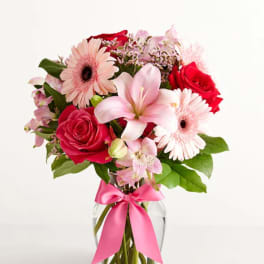 Pink and red flower bouquet in a glass vase with a pink ribbon