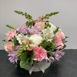 Pastel flower arrangement in a round box with pink, white, and lavender blooms