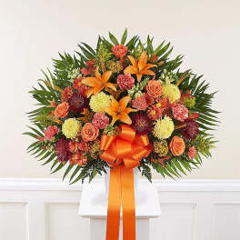 Orange and pink floral standing spray with a ribbon on a white easel