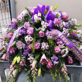 Large purple and pink funeral spray with ribbon on a stand