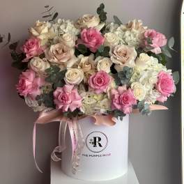 Pink and cream roses with white hydrangeas arranged in a white hatbox with ribbons
