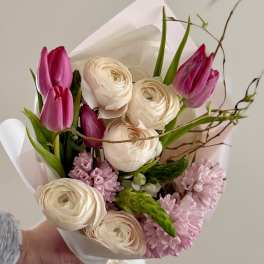 Hand-tied bouquet of pink tulips and cream ranunculus wrapped in white paper