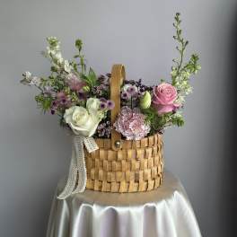 Pastel pink and white flower arrangement in a woven basket on a draped table.