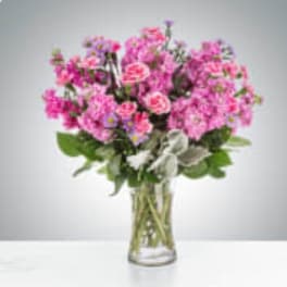 Pink carnation bouquet with small purple filler flowers in a clear glass vase