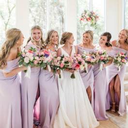Bridesmaids and bride holding pastel flower bouquets indoors