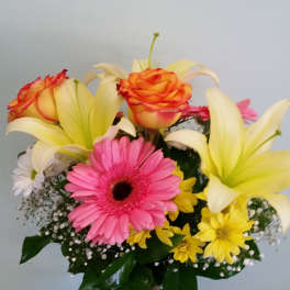Bouquet of lilies, gerbera daisies, roses, and yellow daisies in a glass vase