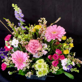Mixed bouquet with pink gerbera daisies, roses, and purple flowers in a low container