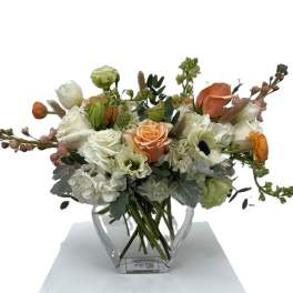 Mixed bouquet of white, peach, and orange flowers in a clear glass vase