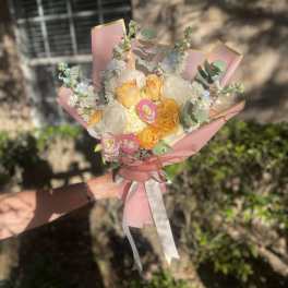 Handheld bouquet of peach, pink, and white flowers wrapped in pink paper