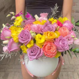 Large bouquet of pink, purple, and yellow flowers in a white round vase