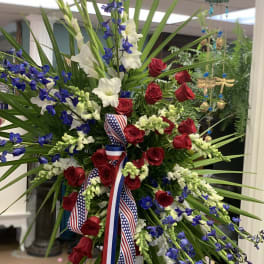 Large standing floral spray with red roses, white flowers, and blue blooms