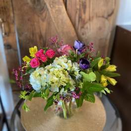 Mixed bouquet of white hydrangeas, pink spray roses, yellow alstroemeria and purple blooms in a glass vase