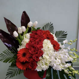 Red roses and gerbera daisies with white orchids in a red vase
