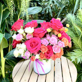 Bright mixed roses arranged in a white hatbox with a pink ribbon