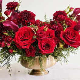 Red roses and burgundy blooms in a gold pedestal vase