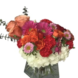 Mixed bouquet of orange, pink, red, and white flowers in a glass vase