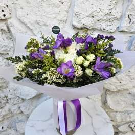 Purple and white bouquet wrapped in paper with a ribbon
