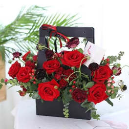 Red roses arranged in a black gift bag with ribbon