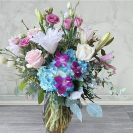 Mixed bouquet of pink, white, and blue flowers in a glass vase