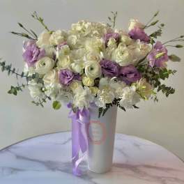 White and lavender bouquet in a tall white vase with a purple ribbon